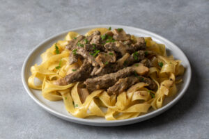Creamy beef and noodles served on a plate, featuring tender beef strips over wide egg noodles, garnished with parsley, representing a quick and easy infused Crock-POT meal.