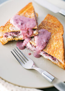 Stuffed French toast with berry sauce on a plate, featuring a fork, highlighting a cannabis-infused breakfast dish.