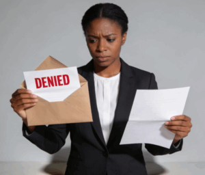 Woman in business attire holding a "DENIED" letter and a document, expressing disappointment, symbolizing challenges faced by cannabis businesses in accessing loans.